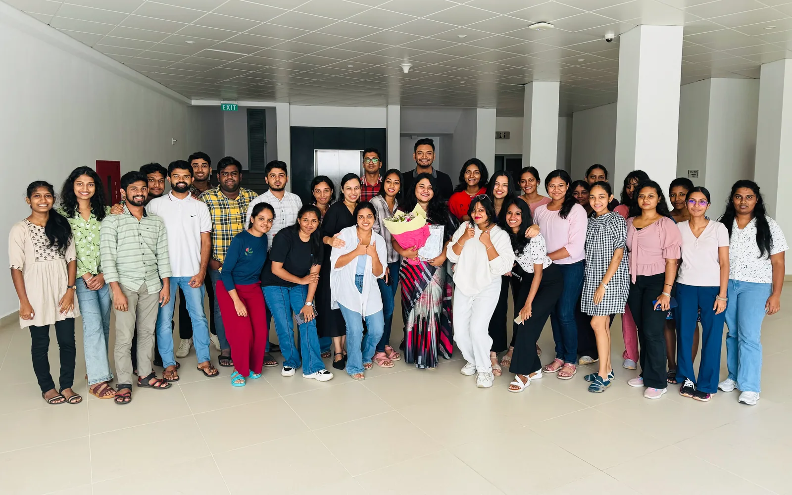 All of Batch 23.1 with a lecturer holding flowers, in a hall on campus. Open it full screen.